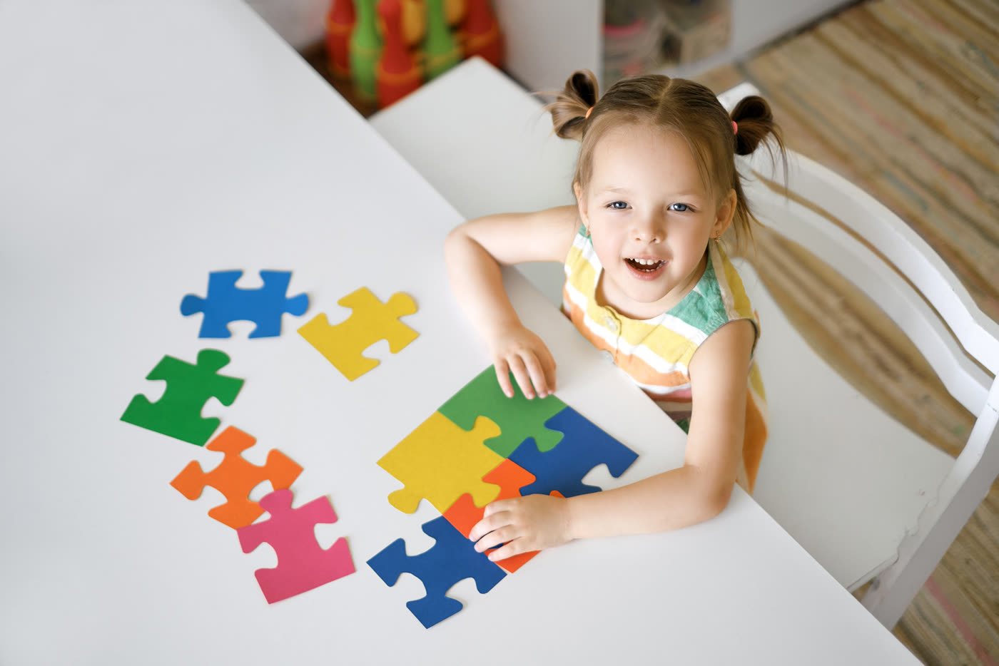 A young girl laughing as she assembles a colourful puzzle